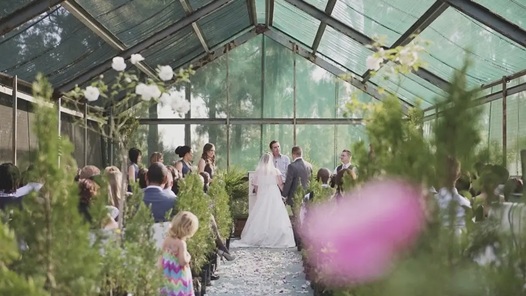 Greenhouse wedding ceremony aisle with guests, florals, and the couple at the altar